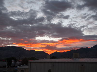 [The tops of the mountains are rimmed with rows of orange which merge with grey then white clouds above the orange.]